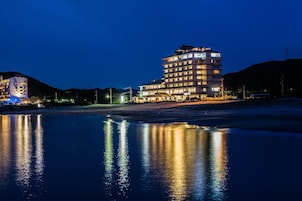 Un hotel de varios pisos con una piscina reflectante en primer plano, rodeado de colinas.