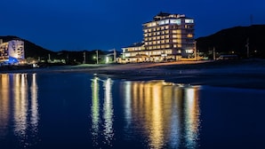 A multi-story hotel with a modern design, located near a body of water reflecting its lights. - Naruto Grand Hotel (Naruto)