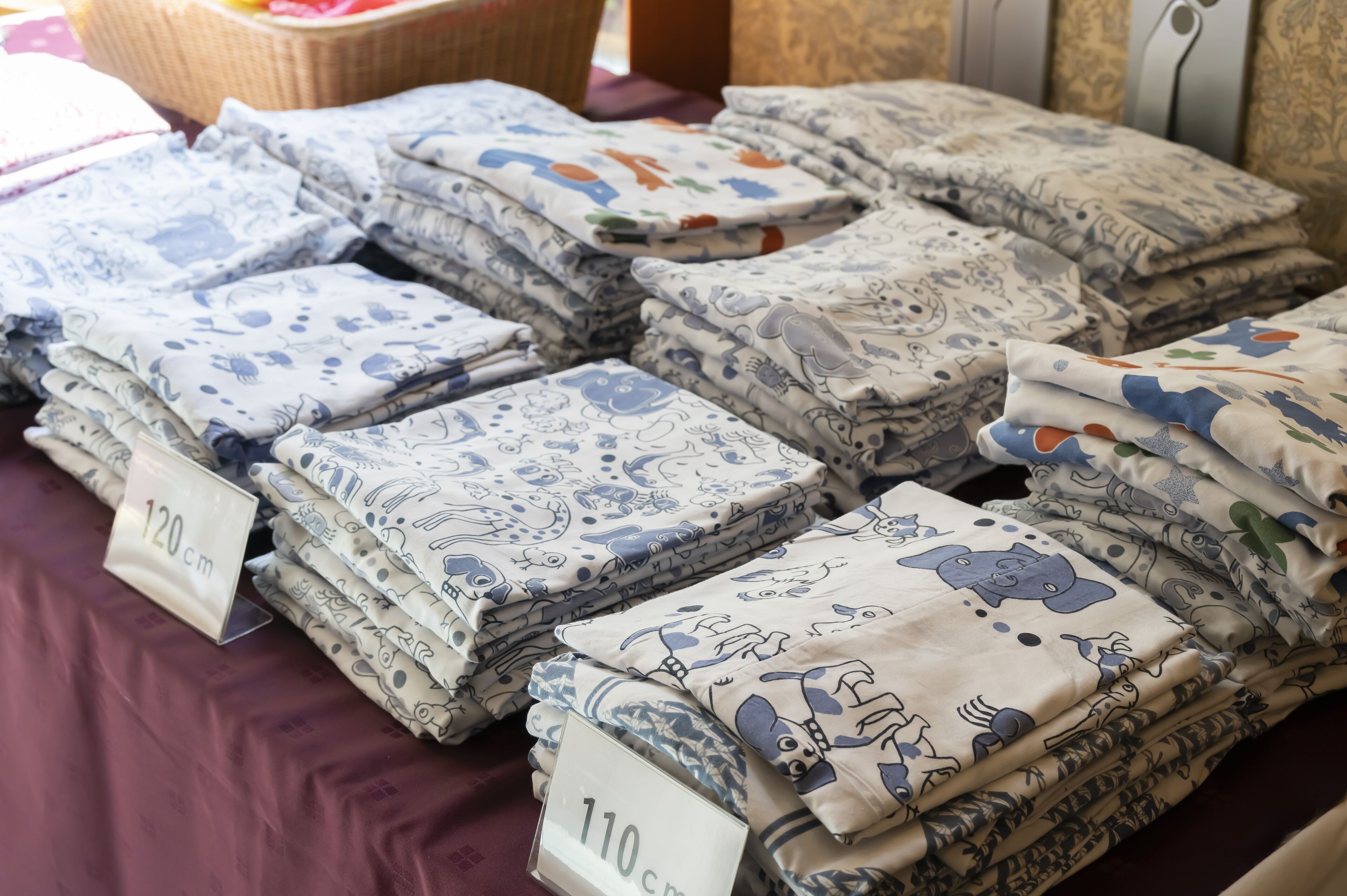 Neatly stacked bedding sets with cartoon prints, labeled with sizes 110 cm and 120 cm.