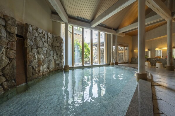 Una amplia piscina interior con paredes de piedra y grandes ventanales que dejan entrar la luz natural.