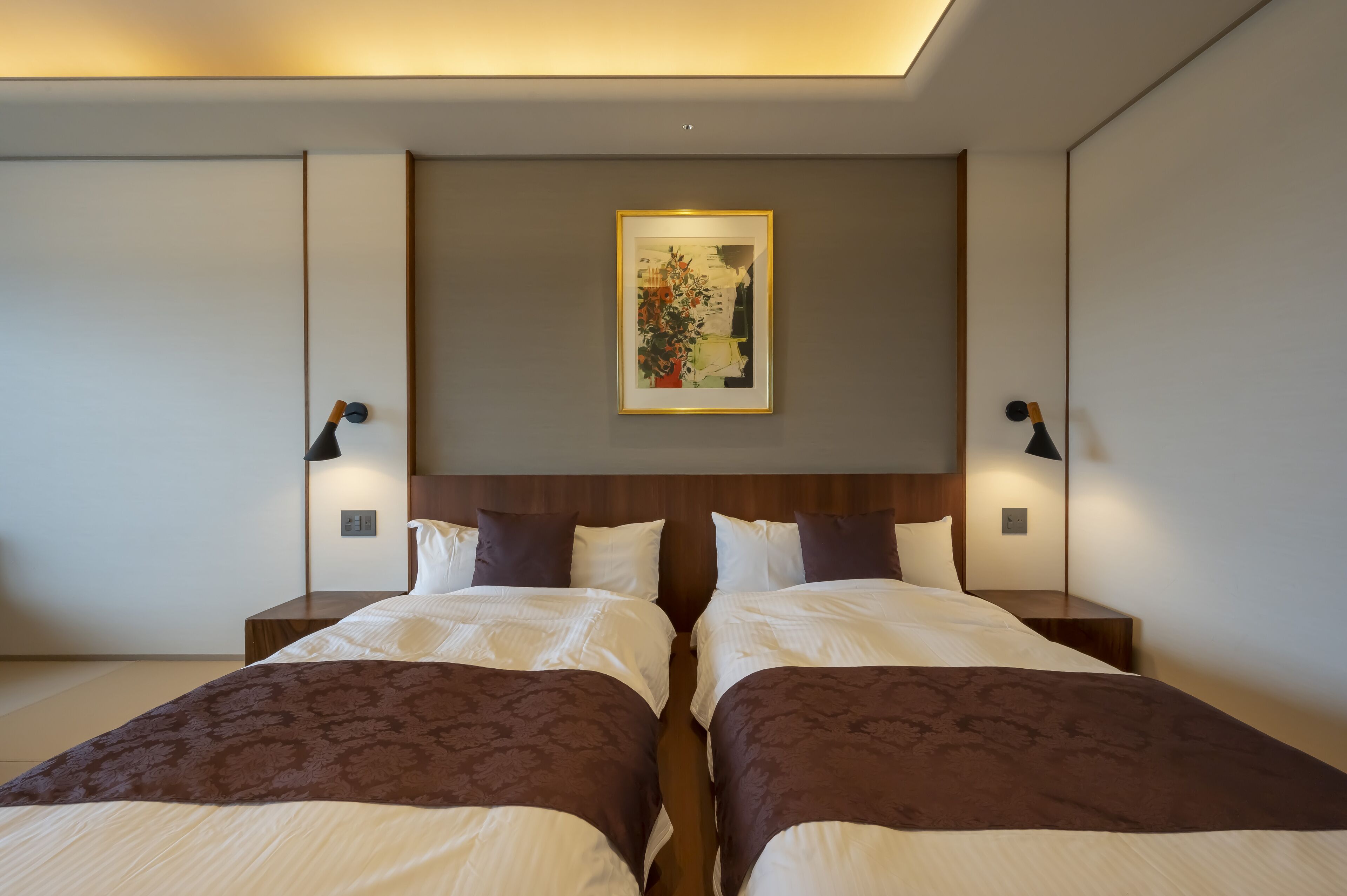 Une chambre d’hôtel moderne avec deux lits, une grande œuvre d’art encadrée au-dessus de la tête de lit et des lampes de chevet.