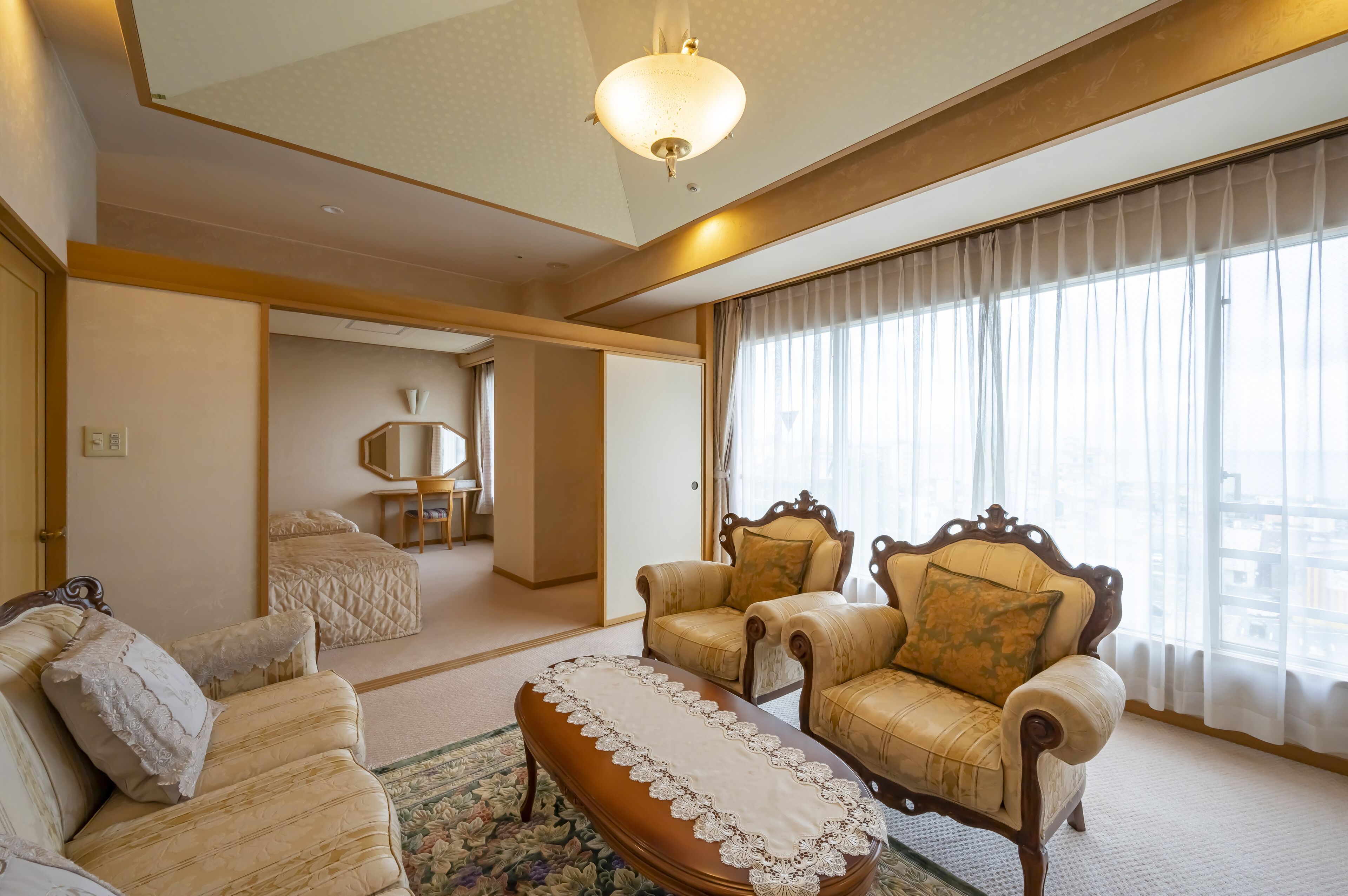 Amplia sala de estar con un ventanal grande, un sofá, dos sillones, una mesa de centro de madera y un tapete decorativo.