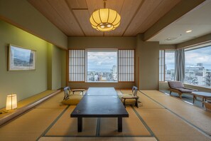 A traditional tatami room with a low table, chairs, and a view of the city through shoji screens. - Kaike Tsuruya (Yonago)