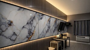 A modern hotel room with a large marble wall, a flat-screen TV, a small table with a remote, and a waste bin. - Grandview Hotel New York (Flushing)