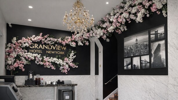 A reception area with a black wall, floral decorations, a chandelier, and a cityscape artwork. - Grandview Hotel New York (Flushing)