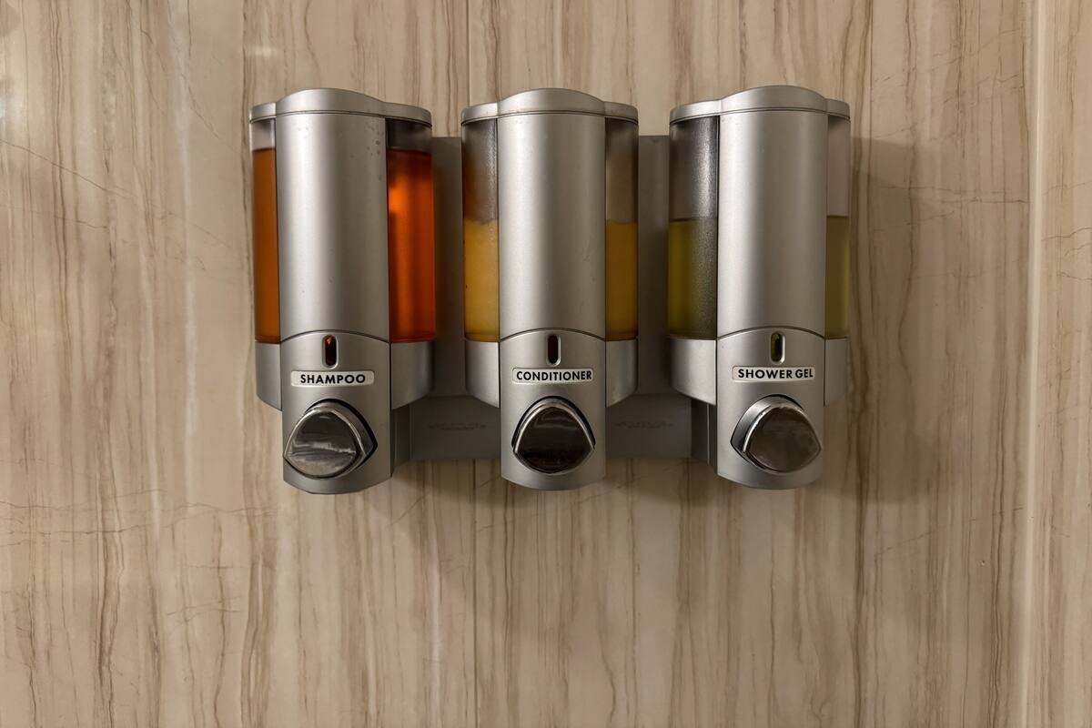 Dispensador fixado na parede com três compartimentos identificados para champô, condicionador e gel de banho.