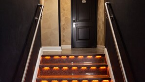 A staircase with illuminated steps and metal handrails, leading to a dark door. - Grandview Hotel New York (Flushing)