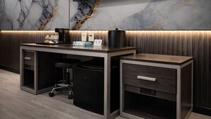 A modern office space with a marble wall, a flat-screen TV, a desk with a coffee machine, and a trash bin. - Grandview Hotel New York (Flushing)