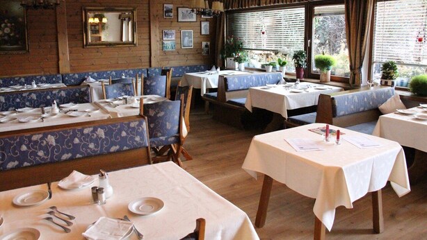 A restaurant with wooden walls, blue patterned booths, and tables set for dining.