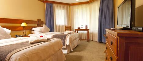 A hotel room with two beds, a wooden dresser, a television, and a small table with a lamp.