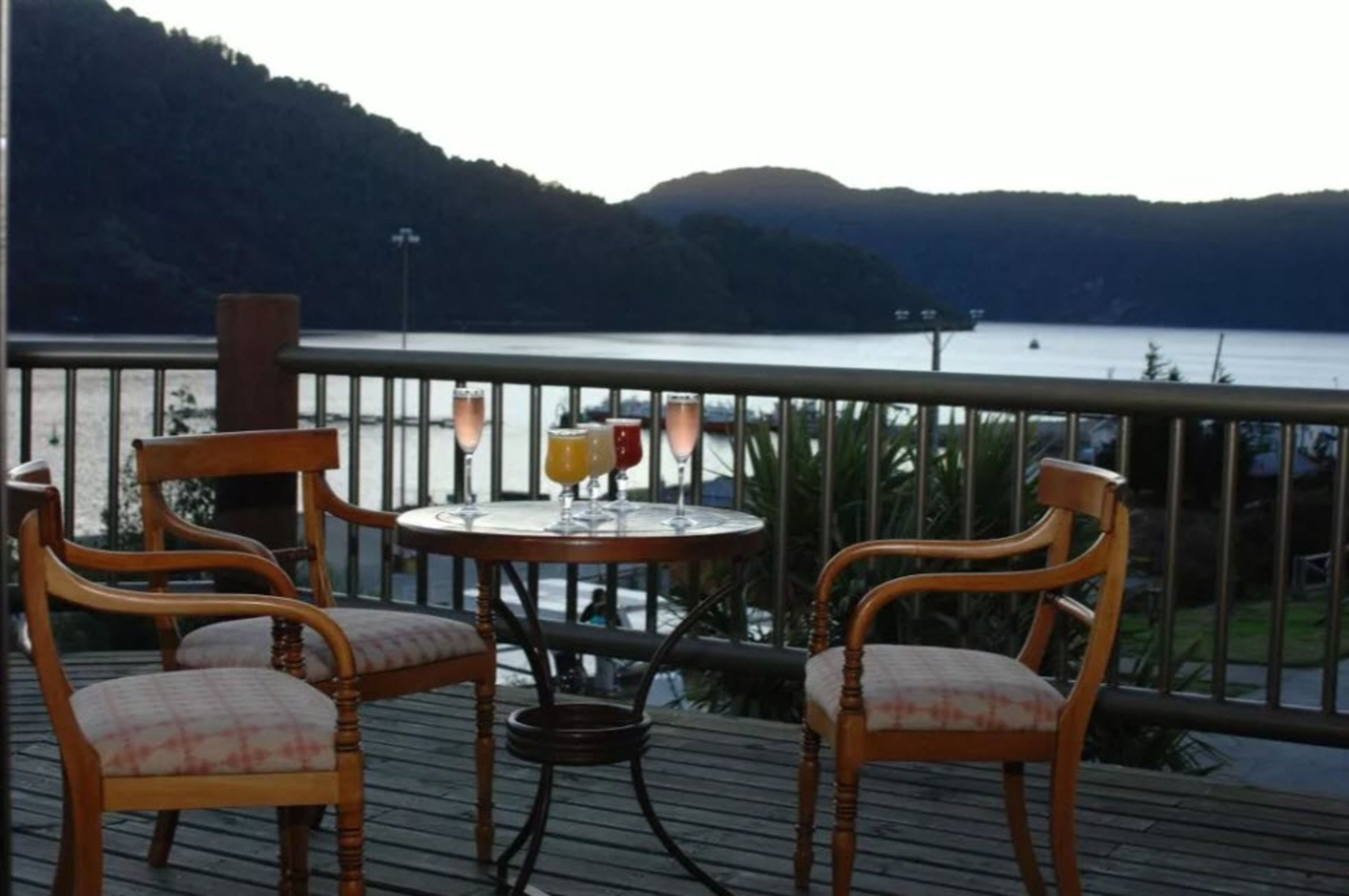 A wooden deck with two chairs and a table, overlooking a lake with mountains in the background.