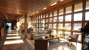Een ruime lobby met een hoge plafond, grote ramen en een centraal zitgedeelte met een bank en stoelen.