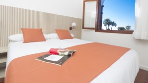 A hotel room with a bed, a window with a view of palm trees, and a wooden headboard. - Alsol Las Orquideas (San Bartolomé de Tirajana)