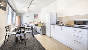 Una cocina moderna con armarios blancos, microondas y refrigerador. Hay un comedor con mesa y sillas.