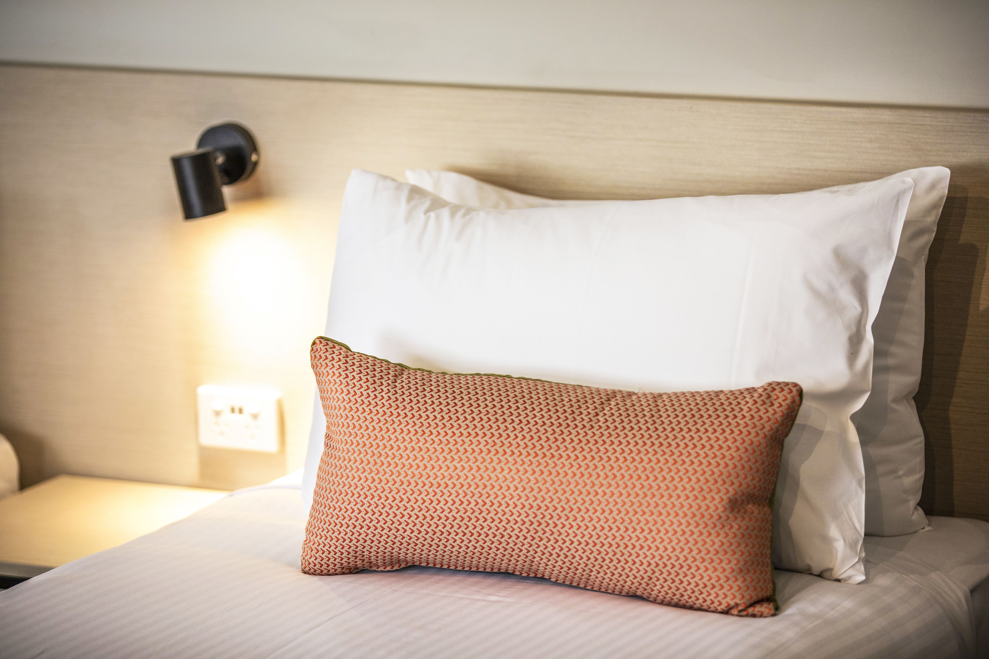 A neatly made bed with two pillows, one patterned and one plain, and a bedside lamp.