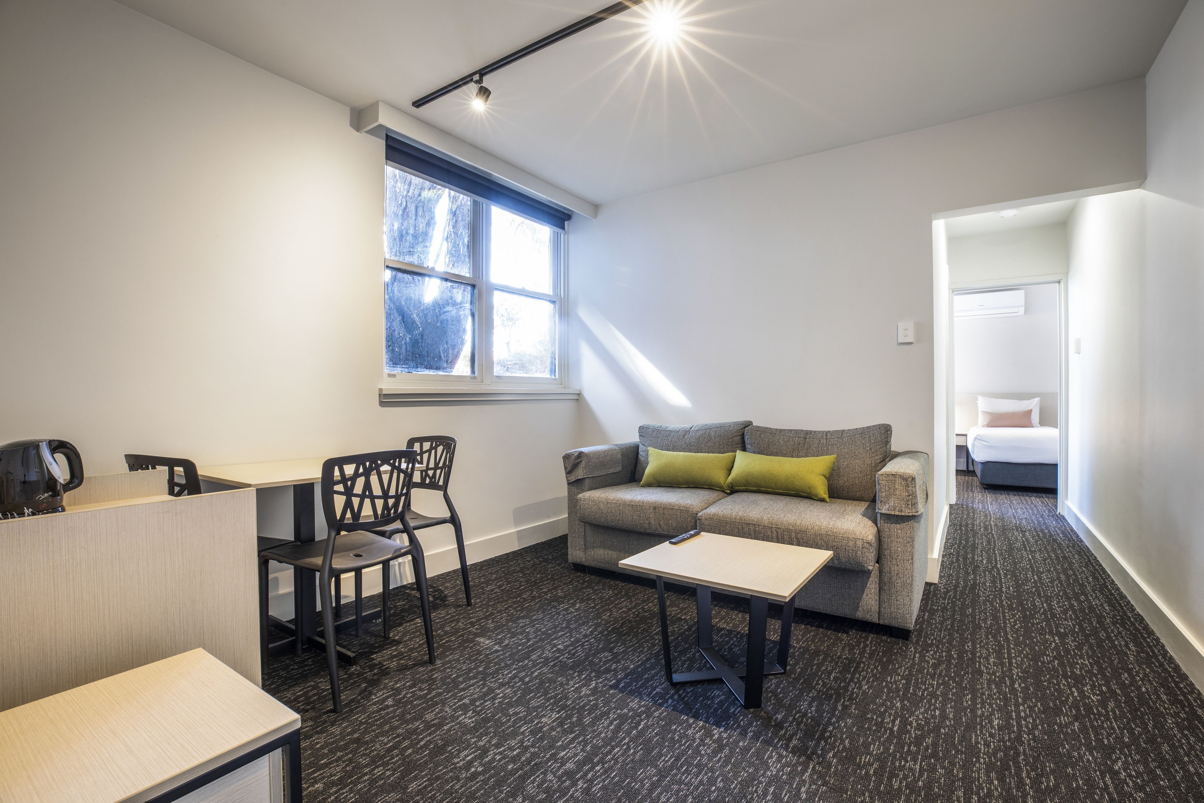 Une chambre d’hôtel moderne équipée d’un canapé, d’une petite table, d’un bureau avec une chaise et d’une fenêtre donnant sur des arbres.