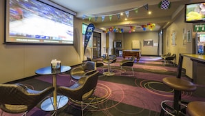 Un salón de conferencias con una pantalla grande mostrando un evento deportivo, diversas disposiciones de asientos y una zona de bar.