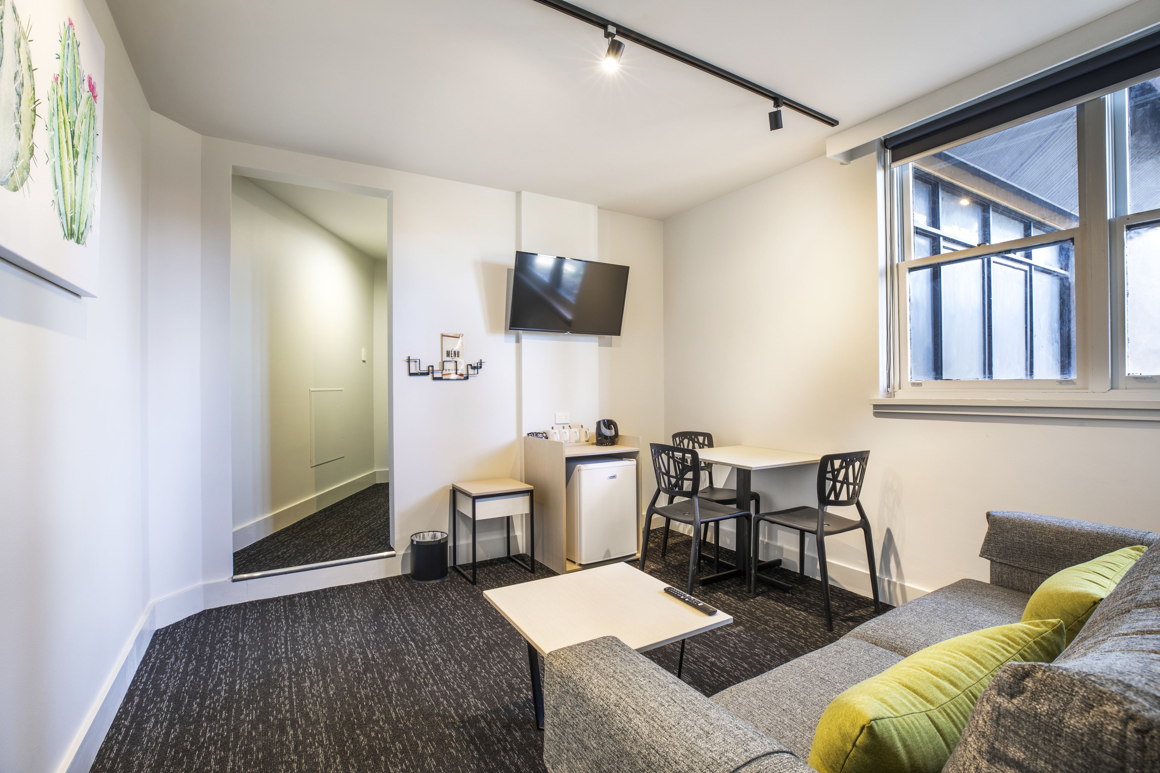 A compact living space with a kitchenette, a flat-screen TV, a sofa, and a window with a view.