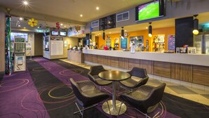 Un hall de hotel con mostrador de recepción, zona de estar y una pantalla de televisión mostrando un evento deportivo.