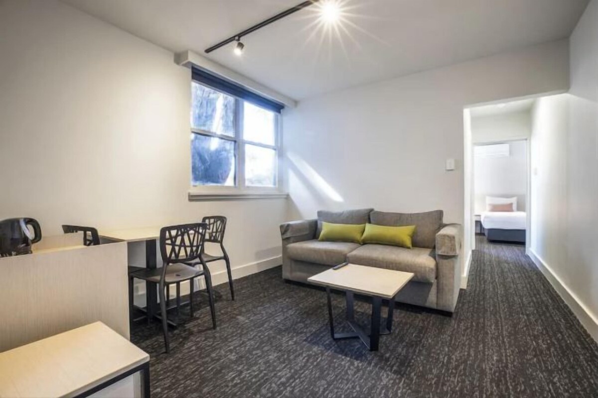 A modern, well-lit room with a sofa, a small table, and a desk with chairs.