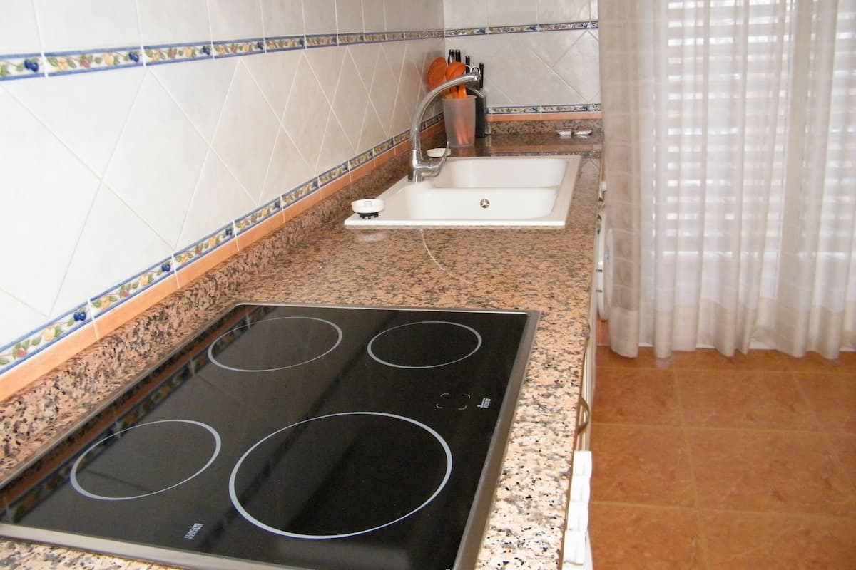 A kitchen with a stove, sink, and tiled backsplash.