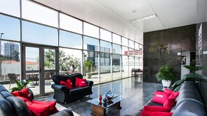 A spacious lobby with large windows, black leather sofas with red cushions, a glass coffee table, and potted plants. - Hotel InterAmericana (Americana)