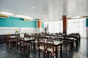 A spacious dining area with multiple tables and chairs, a kitchen area with a counter, and a large window providing natural light. - Hotel InterAmericana (Americana)
