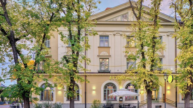 A historic building with a cafe on the ground floor, outdoor seating, and a staircase leading to the entrance. - Grand Hotel Glorius (Mako)
