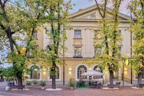 A historic building with a cafe on the ground floor, outdoor seating, and a staircase leading to the entrance. - Grand Hotel Glorius (Mako)
