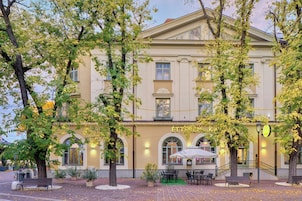 Un edificio histórico con una cafetería en la planta baja, mesas al aire libre y una escalera que conduce a la entrada.