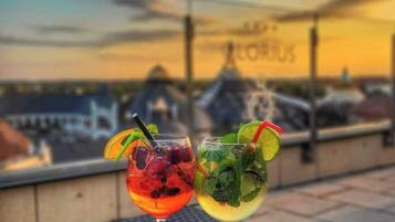 Two cocktails on a table with a view of a building and a sunset in the background.