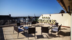 A rooftop terrace with outdoor seating and a view of city buildings. - Grand Hotel Glorius (Mako)