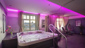 A modern spa room with a hot tub, a window with curtains, a hanging chair, and a potted plant. - Grand Hotel Glorius (Mako)