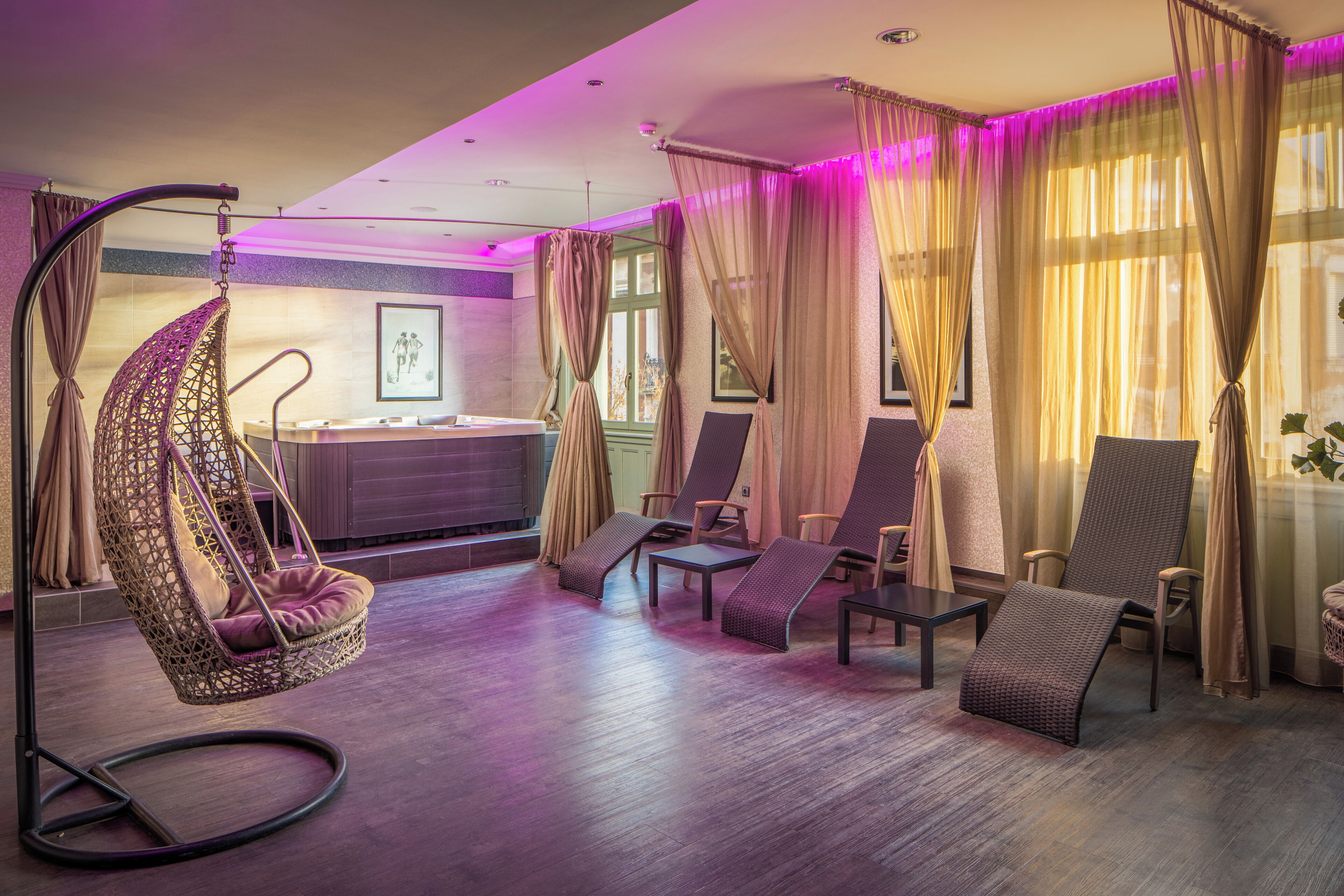 A room with a hanging chair, several lounge chairs, a reception desk, and large windows with sheer curtains.