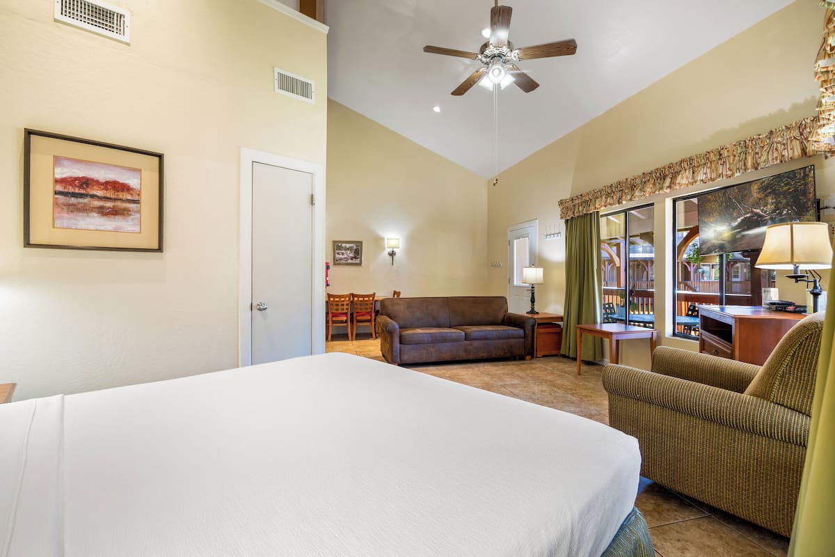 A hotel room with a large bed, a sofa, a chair, a desk, and a ceiling fan.