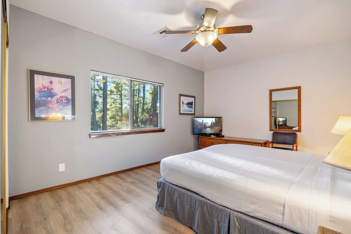 A bedroom with a bed, a ceiling fan, a television, and a window with blinds.