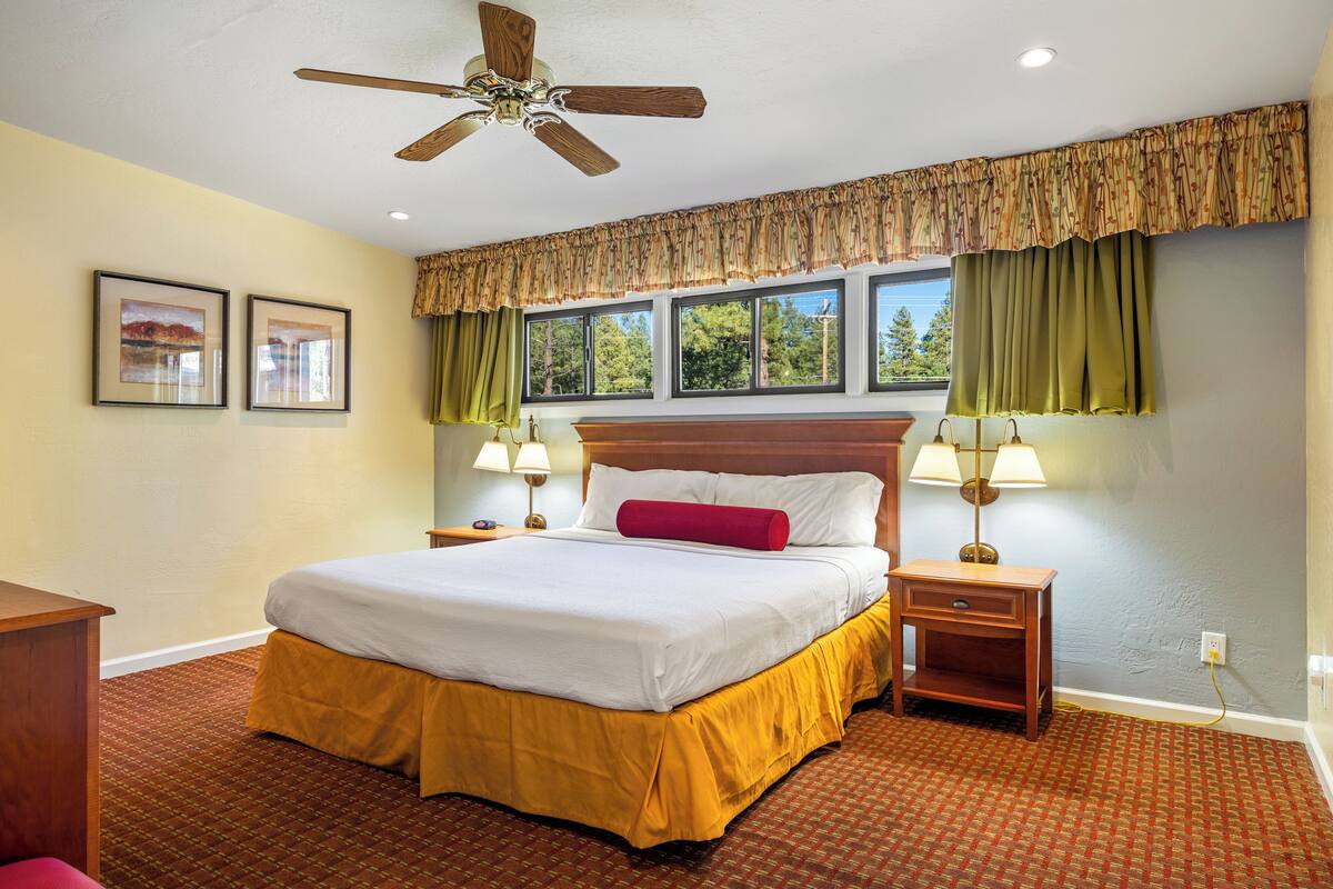 A hotel room with a large bed, two bedside tables with lamps, a ceiling fan, and a window with curtains.