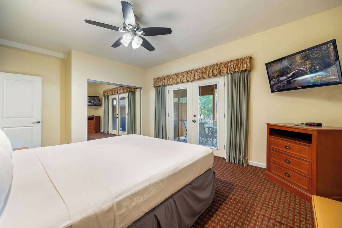 A hotel room with a bed, a TV, a desk, and a view of the outdoors.
