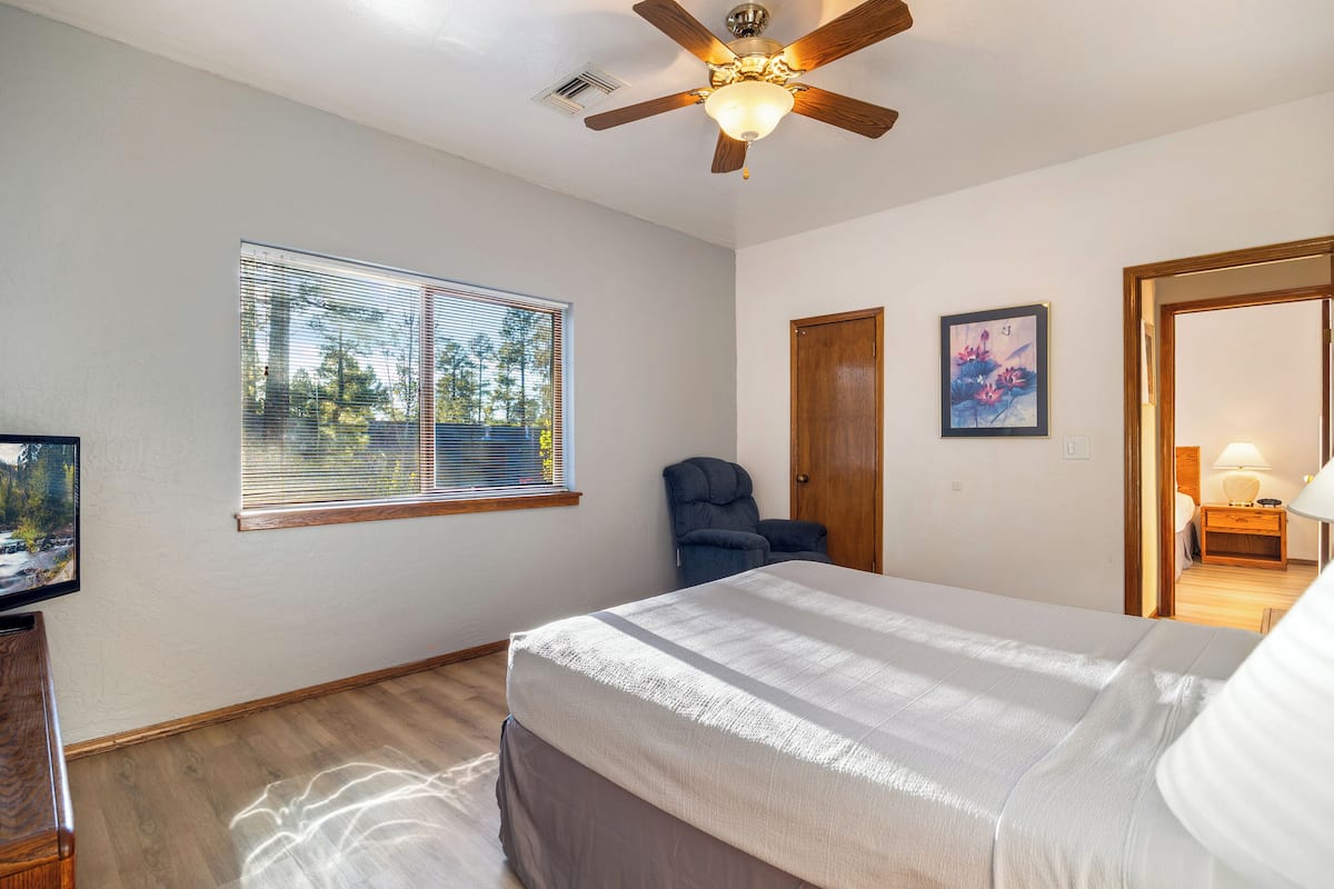 A bedroom with a bed, a ceiling fan, a window with blinds, a door, and a framed picture on the wall.