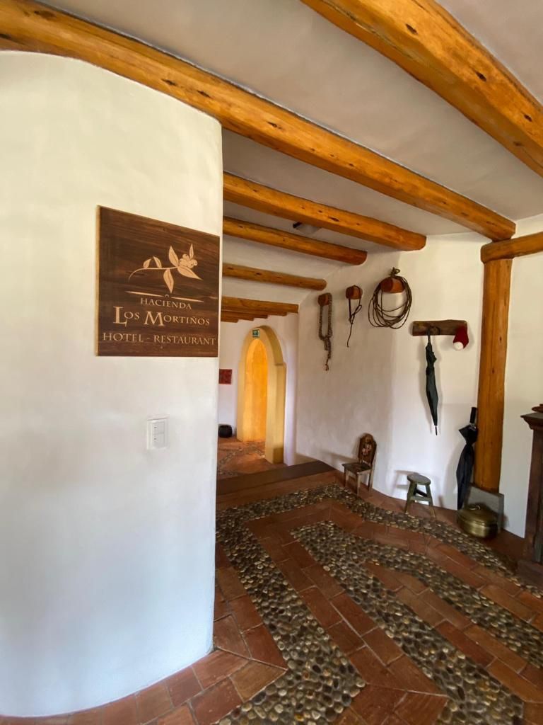 A hallway with a wooden ceiling, a sign for 'Hacienda Los Mortinos Hotel - Restaurant,' and a patterned floor.