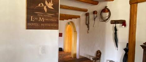 A hallway with a wooden ceiling, a sign for 'Hacienda Los Mortinos Hotel - Restaurant,' and a patterned floor.