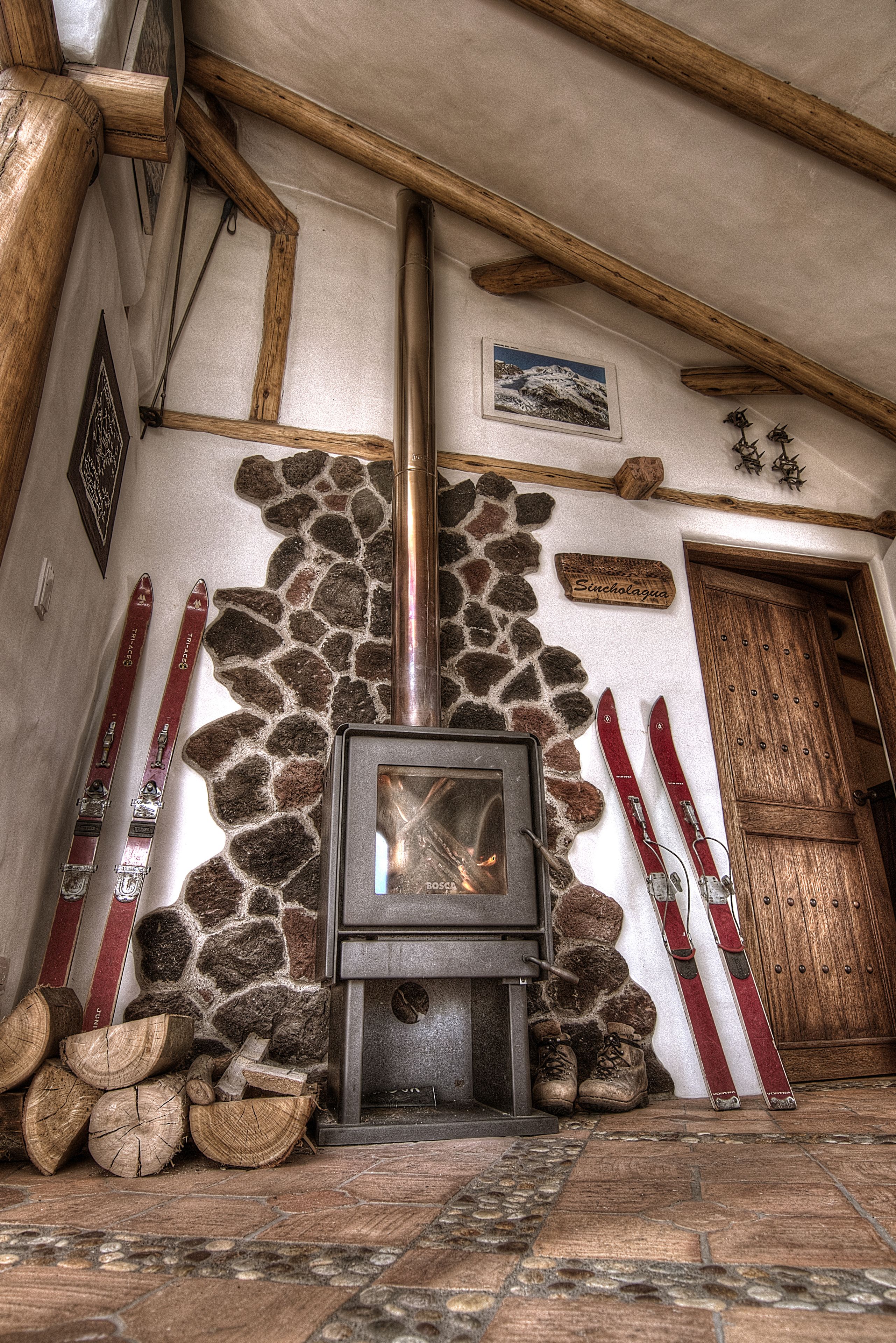 Une cheminée en pierre avec un plafond en bois, des paires de skis appuyés contre le mur et une porte en bois.