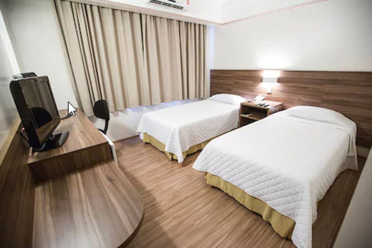 Ein Hotelzimmer mit zwei Betten, einem Schreibtisch mit Computer, einem Stuhl und einem Fernseher.