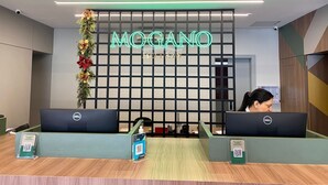 Un comptoir d’accueil avec une enseigne au néon indiquant « MOGANO HOTELS » et deux ordinateurs Dell.