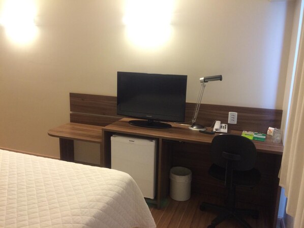 Habitación de hotel con una cama, un escritorio con televisor, una lámpara de escritorio, un teléfono y un cubo de basura.