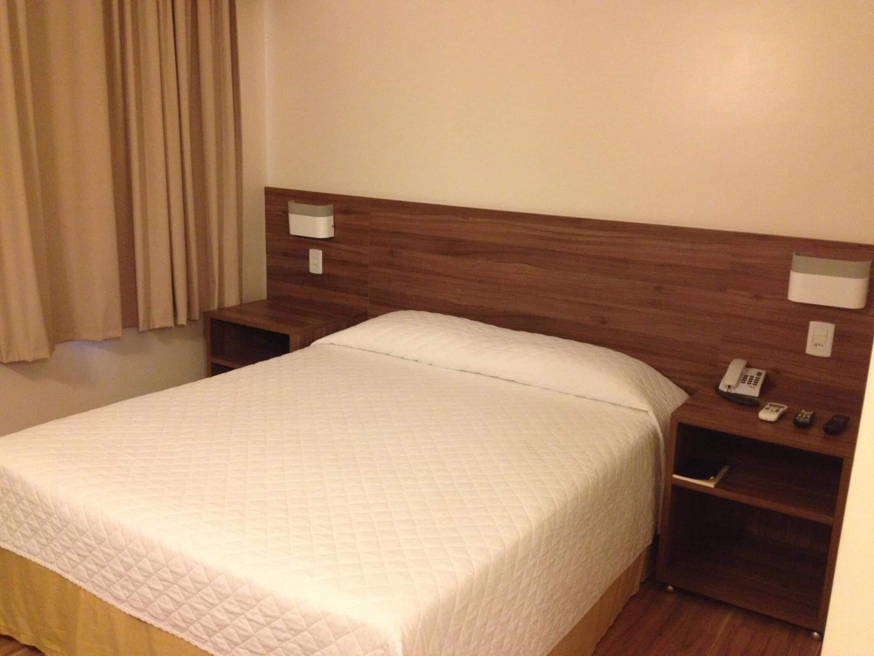 A hotel room with a large bed, wooden headboard, bedside tables with lamps, and a telephone.