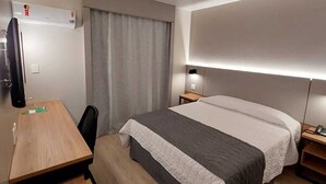 Une chambre d’hôtel comprenant un lit, un bureau, une chaise, une télévision et une table de chevet.