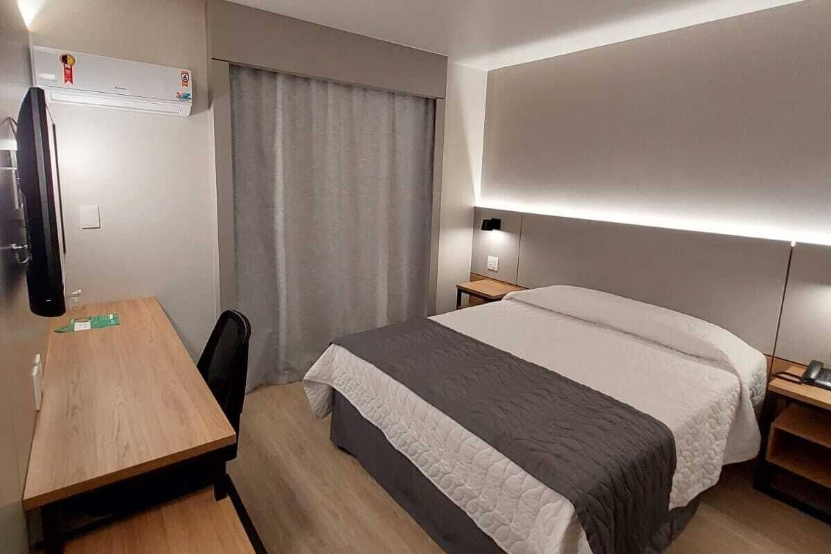 Ein Hotelzimmer mit Bett, Schreibtisch, Sessel, Fernseher und Nachttisch.