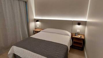 Una habitación de hotel moderna con una cama grande, mesitas de noche e iluminación integrada.