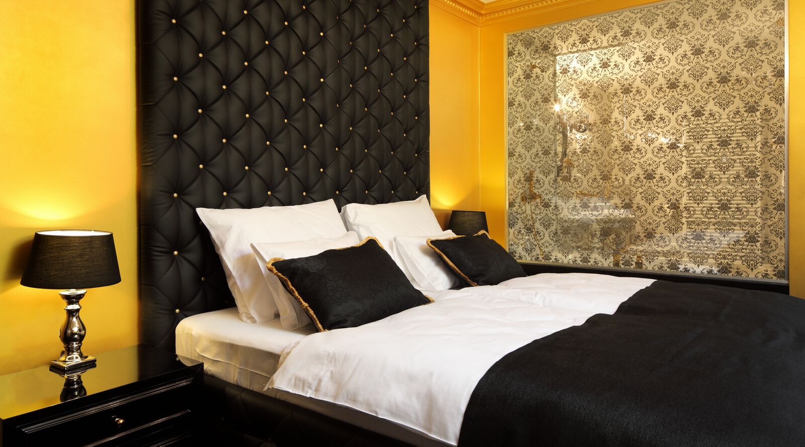 A bedroom with a tufted headboard, a large mirror, and a patterned wallpaper.